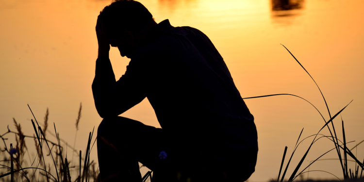 depressed man sitting against the light reflected in the water