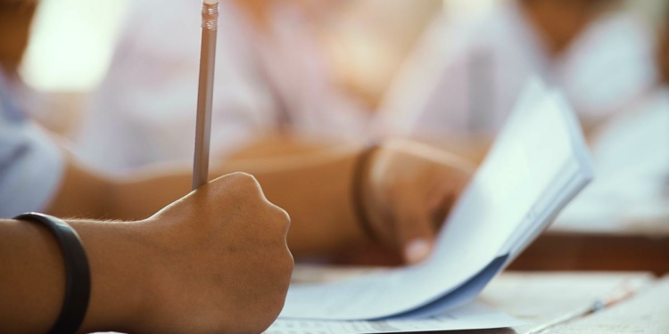 Closeup to hand of student  holding pencil and taking exam in classroom with stress for education test.