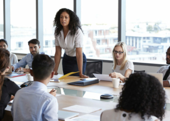 Businesswoman Stands To Address Meeting Around Board Table