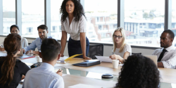 Businesswoman Stands To Address Meeting Around Board Table